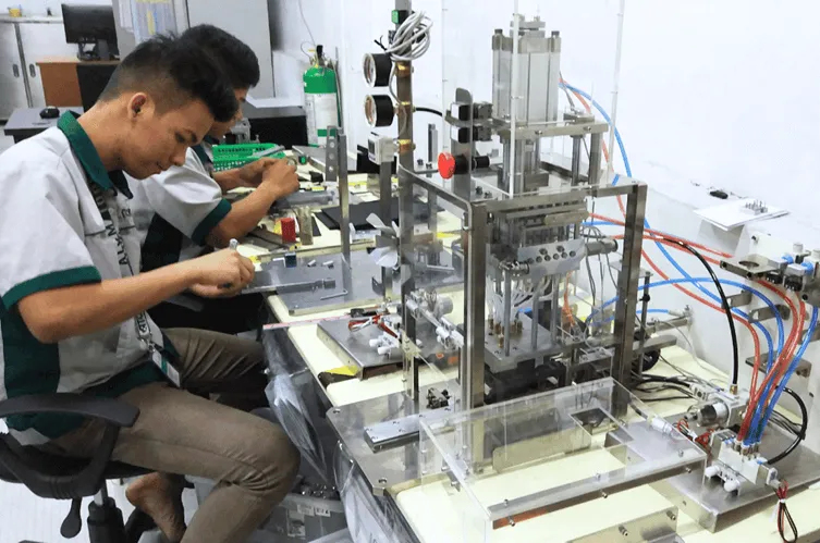 Technicians assembling a semi-automated production jig with a pneumatic press and control wiring at the workbench