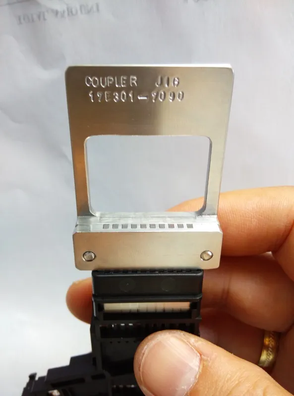 Machined aluminum coupler jig held up for inspection beside its connector assembly